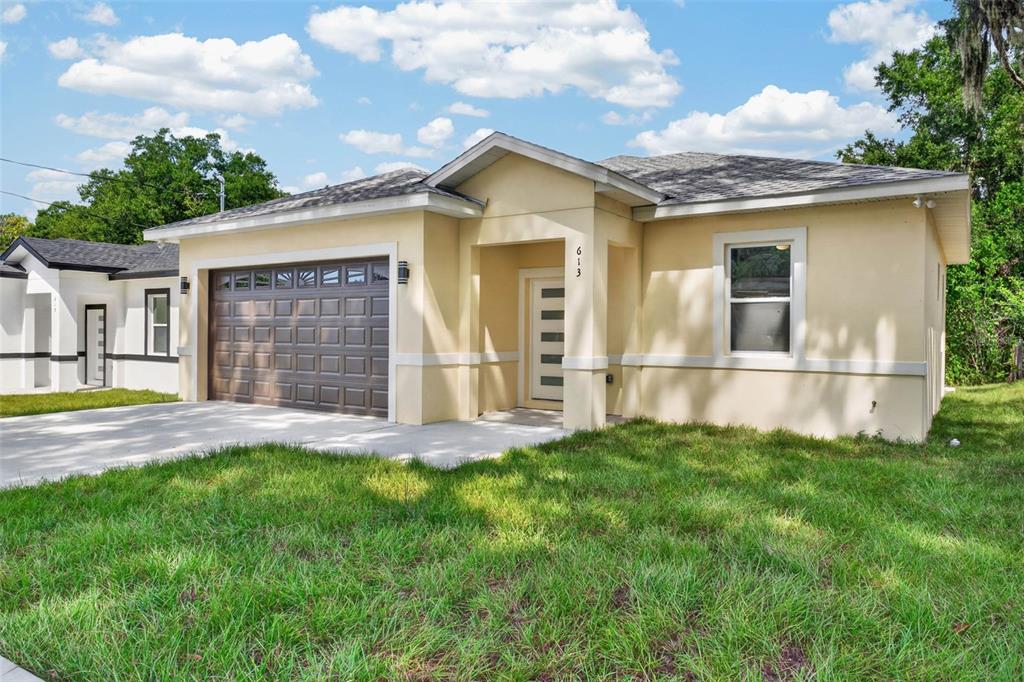 A single-story house with a tan stucco exterior, a brown garage door, and a front entrance — 613 W VALENCIA STREET, LAKELAND, FL