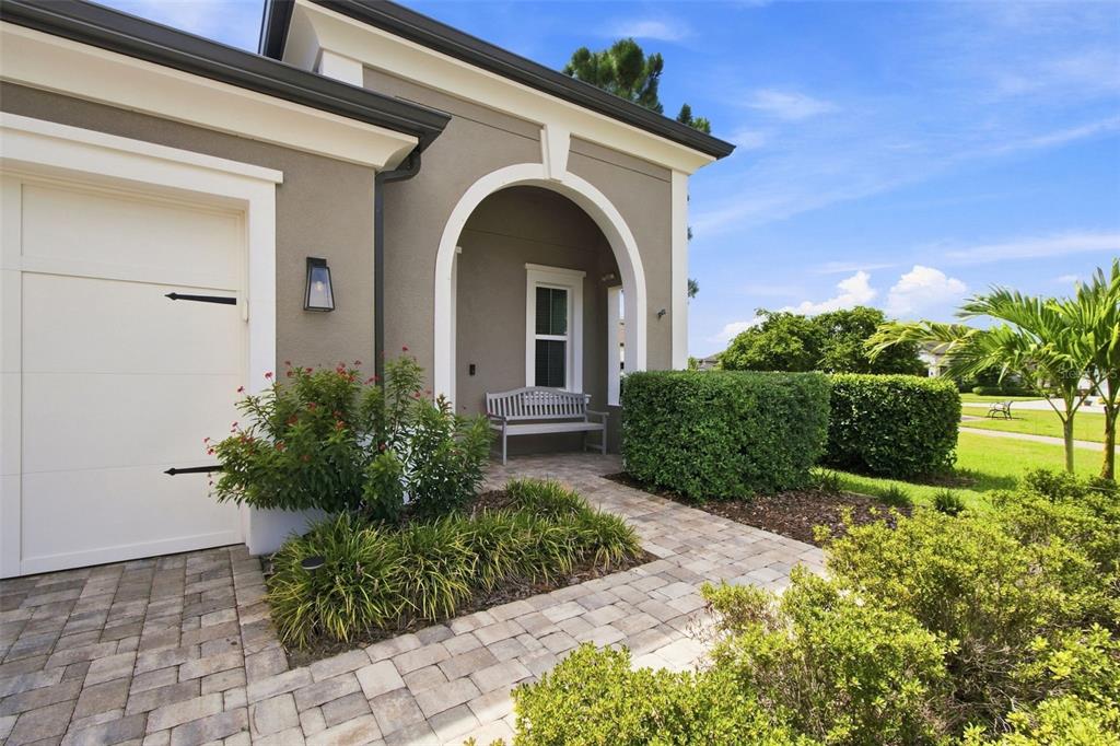 A paved walkway leads to a covered entryway with an arched opening and a wooden bench — 4623 BARLETTA COURT, WESLEY CHAPEL, FL