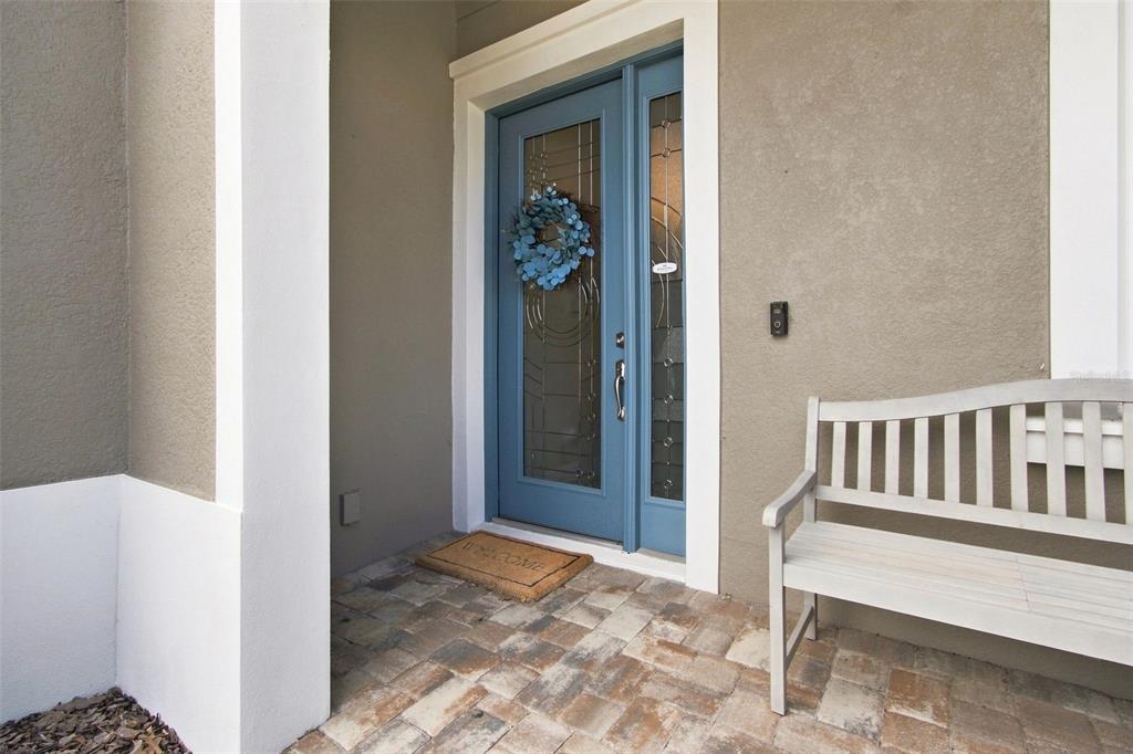A blue front door with a glass insert and a wreath sits beside a wooden bench — 4623 BARLETTA COURT, WESLEY CHAPEL, FL