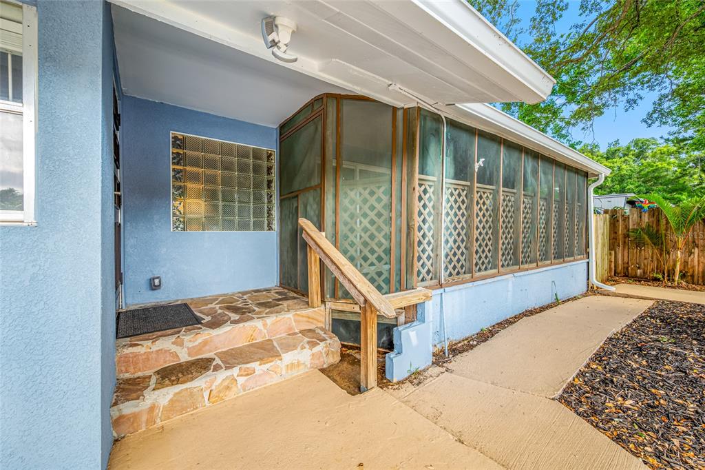 A blue house exterior features a stone-tiled porch, a glass block window, and a screened-in porch — 5044 BETTY STREET N, ST PETERSBURG, FL