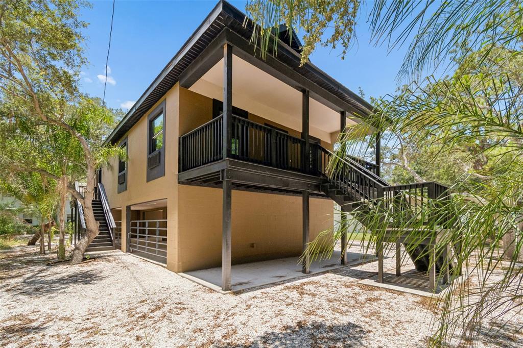An elevated house with a tan exterior, black trim, and a wooden staircase leading upstairs — 16288 48TH ST N, CLEARWATER, FL