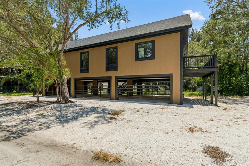A two-story house with a tan exterior, dark trim, and an open ground-level barn area — 16288 48TH ST N, CLEARWATER, FL