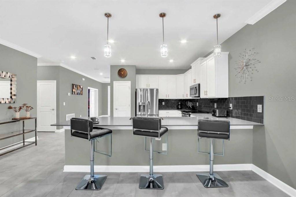 A modern kitchen features white cabinets, gray walls, a breakfast bar, and three bar stools — 3000 PENELOPE LOOP, KISSIMMEE, FL