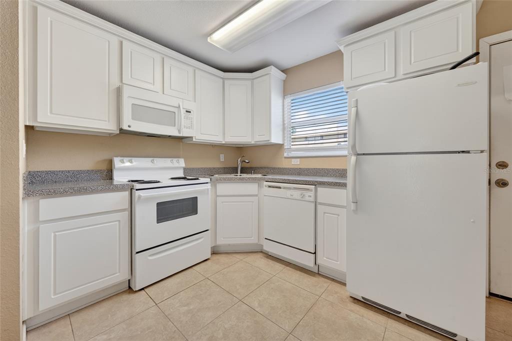 An open-concept kitchen and living area features beige tile flooring, peach walls, and white cabinetry — 4420 CARTER ROAD UNIT 41, ST AUGUSTINE, FL