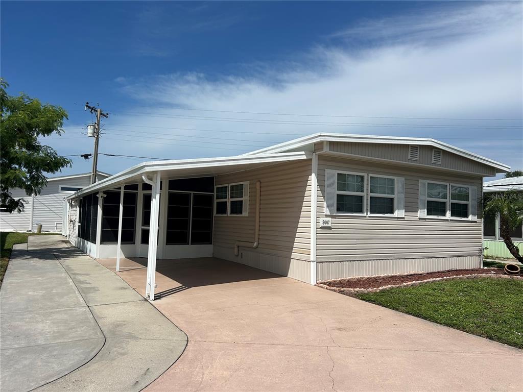 A beige mobile home with a screened-in porch and a concrete driveway under a blue sky — 5007 BOCA RATON AVENUE, SARASOTA, FL