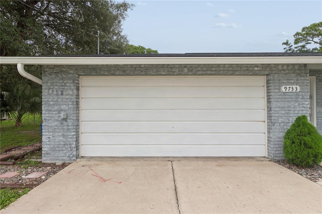 A white garage door is set into a gray brick exterior wall with a concrete driveway — 9733 DICK STREET, HUDSON, FL