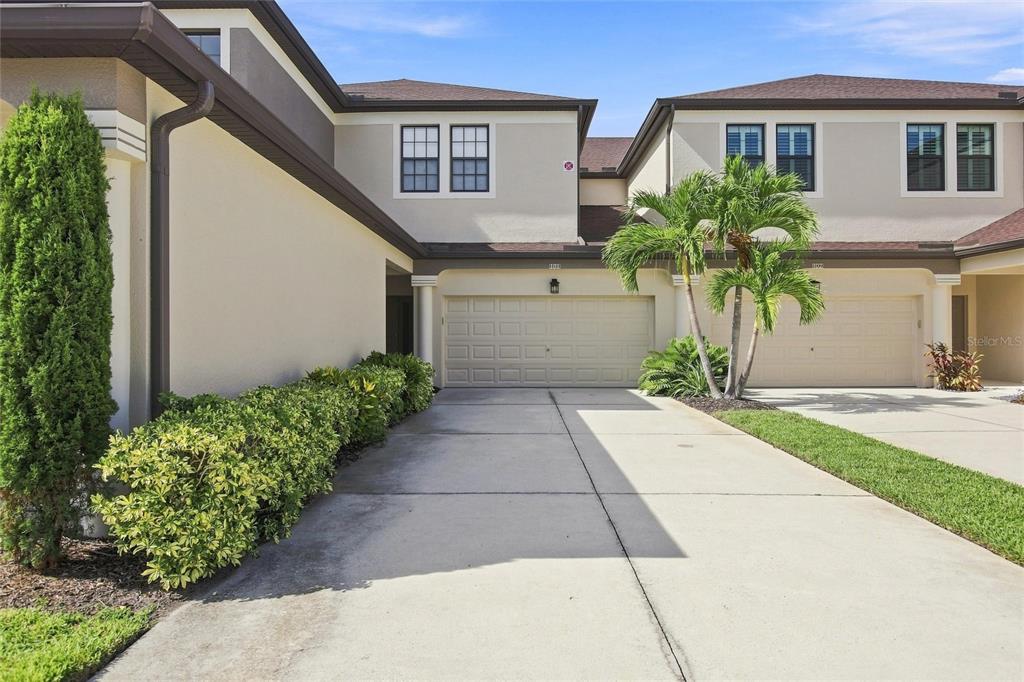 A two-story townhouse exterior features a beige stucco facade, two garage doors, and landscaping — 3781 COSTA MAYA WAY UNIT 101, ESTERO, FL