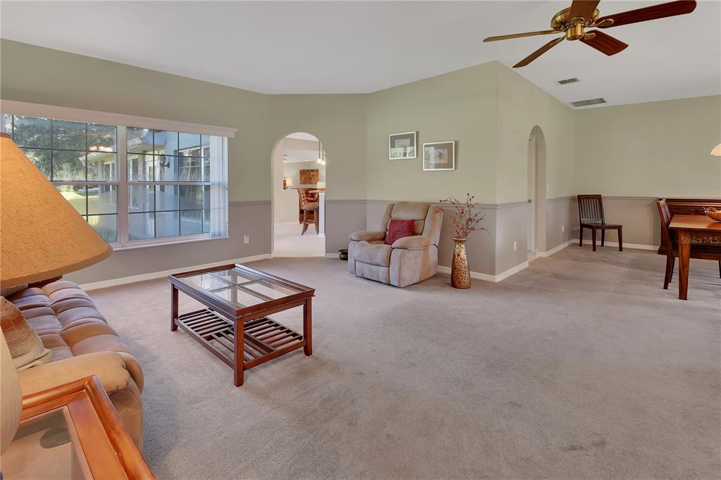 A living room with beige carpet, a recliner, a coffee table, and a dining area — 1925 GLENWOOD OAKS LANE, DELAND, FL