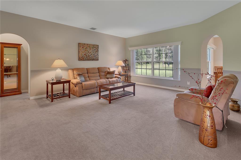 A living room features beige carpet, a tan sofa, a recliner, and a large window — 1925 GLENWOOD OAKS LANE, DELAND, FL