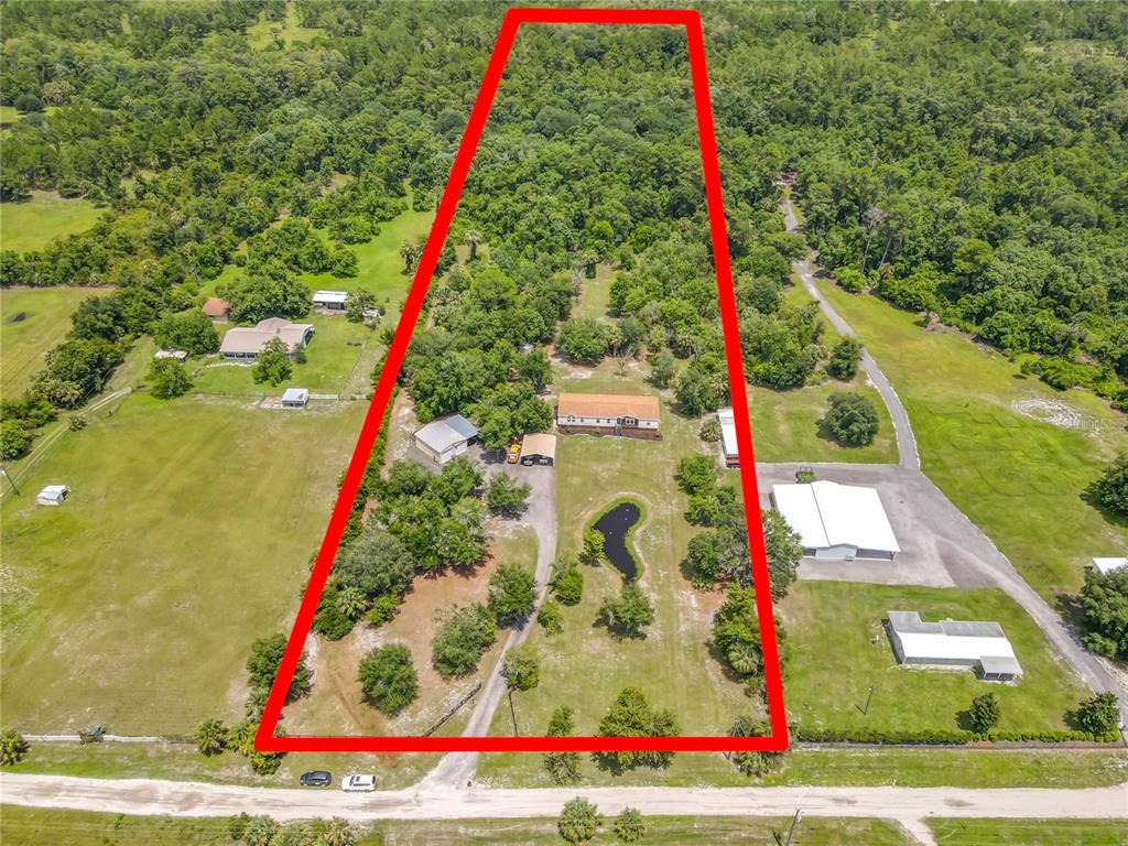 An aerial view shows a house, outbuildings, and a pond on a large, wooded lot — 353 URANUS TRAIL, OSTEEN, FL