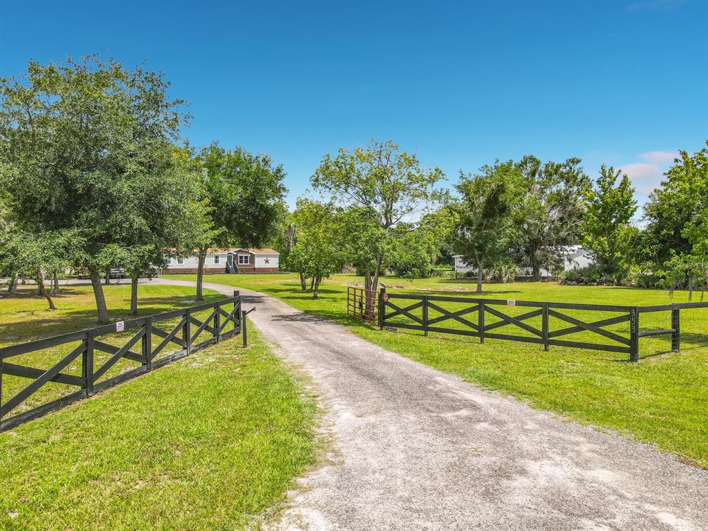A gravel driveway leads through a black wooden fence toward a house among trees — 353 URANUS TRAIL, OSTEEN, FL