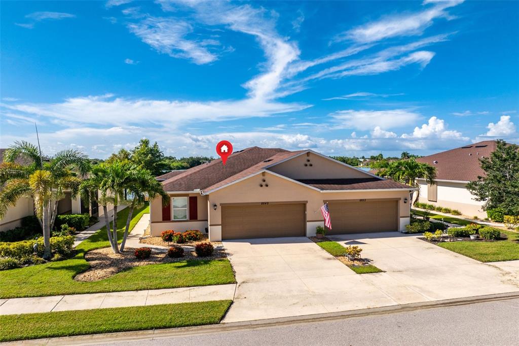 An exterior view of a tan, single-story duplex home with two garages and a shingled roof — 8849 TUSCANY ISLES DRIVE, PUNTA GORDA, FL