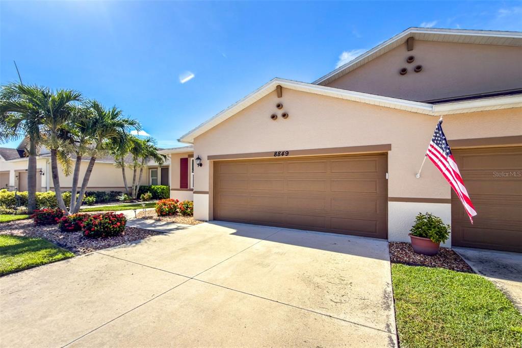 A beige house exterior features a two-car garage, a concrete driveway, and an American flag — 8849 TUSCANY ISLES DRIVE, PUNTA GORDA, FL