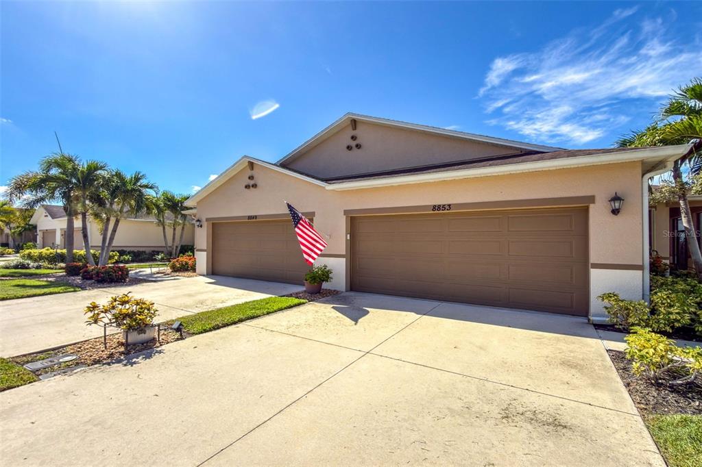 A beige house exterior features a three-car garage and an American flag near the entrance — 8849 TUSCANY ISLES DRIVE, PUNTA GORDA, FL