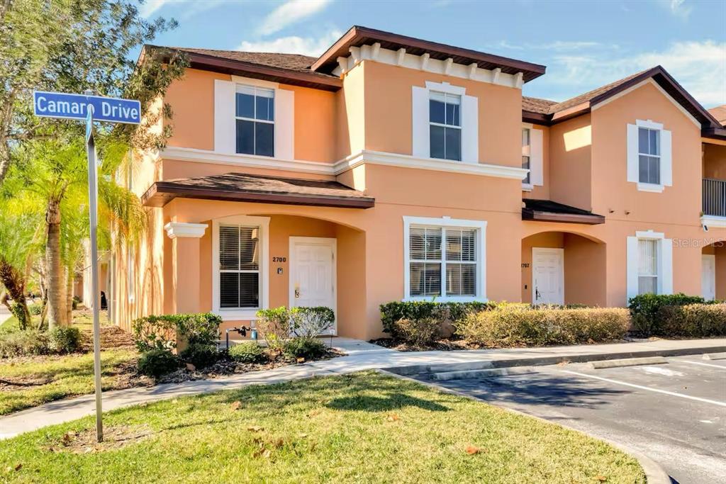 A two-story peach-colored townhouse exterior with a white front door and a street sign — 2700 CAMARO DRIVE, KISSIMMEE, FL