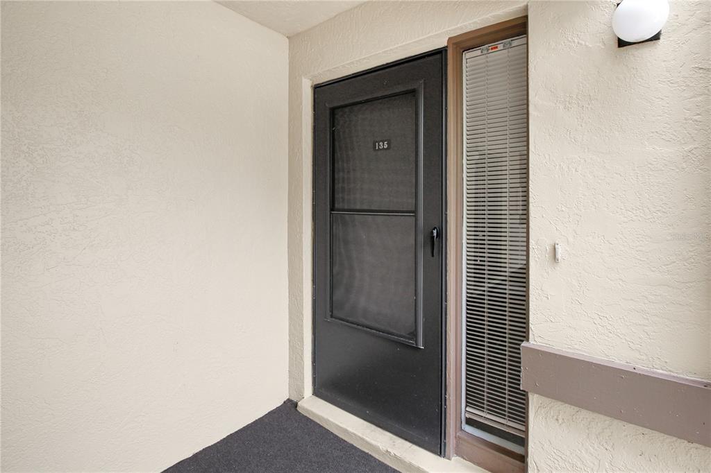 A black screen door with the number 135 leads into a residence with a side window — 135 WOODLAKE WYNDE UNIT 135, OLDSMAR, FL