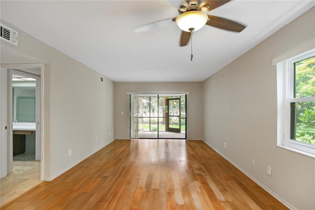 An empty living room with hardwood floors, a ceiling fan, and a sliding glass door — 135 WOODLAKE WYNDE UNIT 135, OLDSMAR, FL