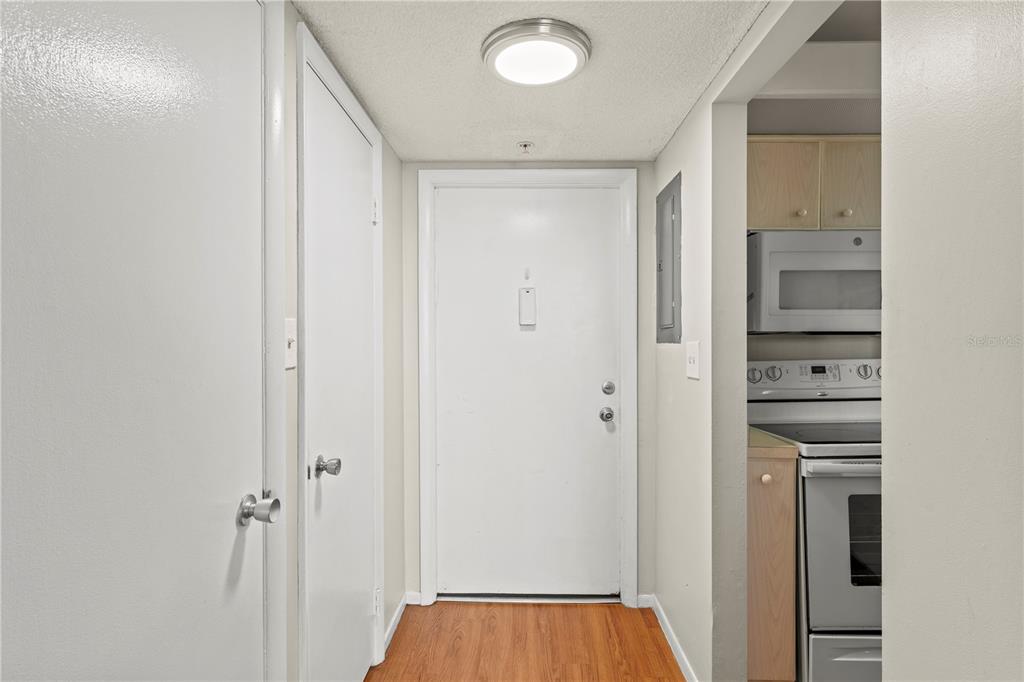 A hallway with wood-look flooring leads to a white front door and a kitchen area — 2020 N ATLANTIC AVENUE UNIT 610N, COCOA BEACH, FL