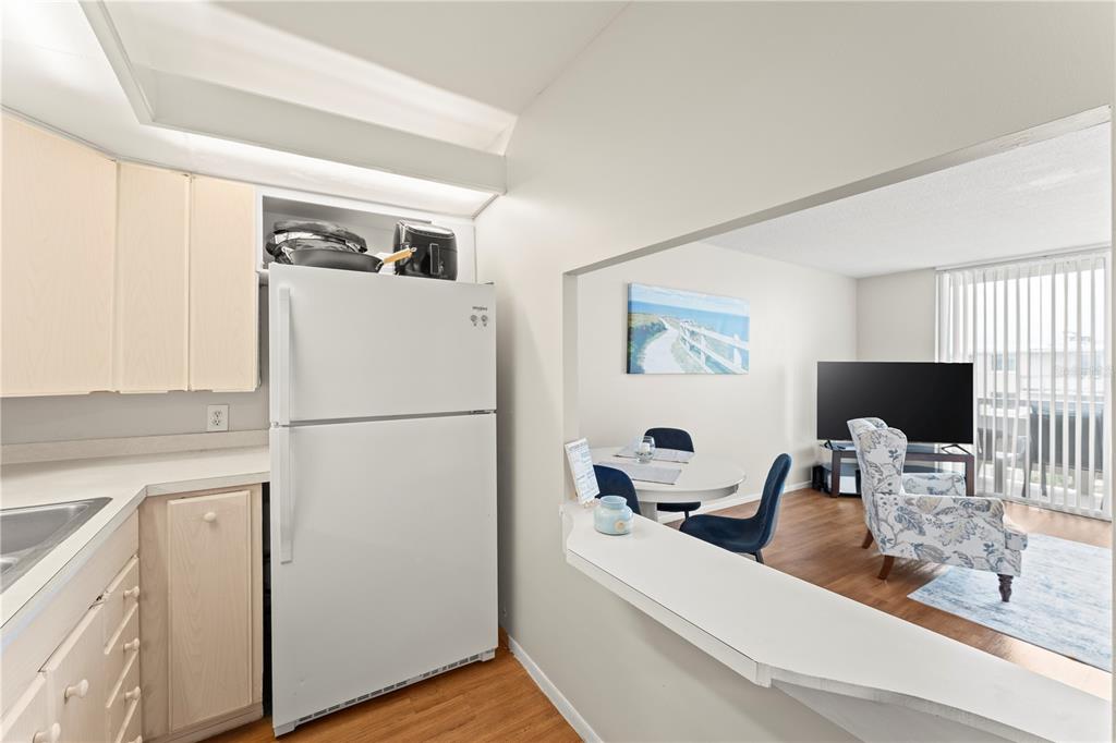 A kitchen with light wood cabinets and a white refrigerator overlooks a living area — 2020 N ATLANTIC AVENUE UNIT 610N, COCOA BEACH, FL