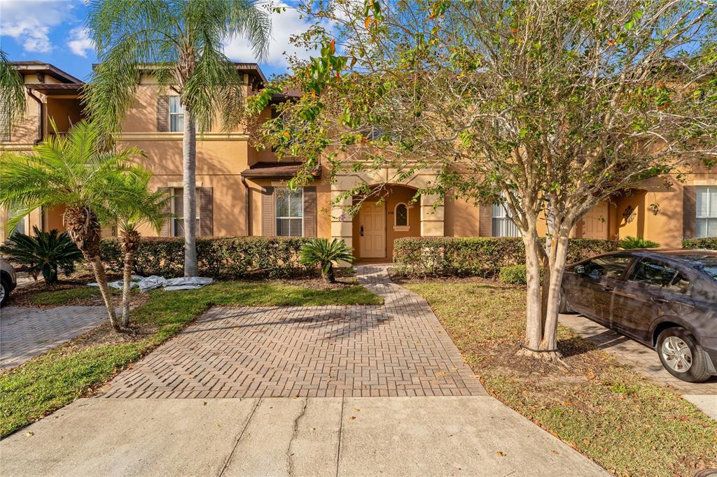 A two-story tan stucco townhouse features a brick paver driveway and a front entrance walkway — 436 CALABRIA AVENUE, DAVENPORT, FL