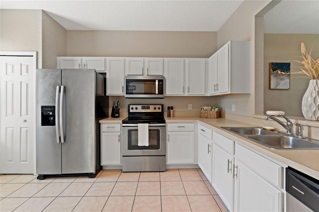 A kitchen features white cabinets, stainless steel appliances, and light-colored tile flooring — 436 CALABRIA AVENUE, DAVENPORT, FL