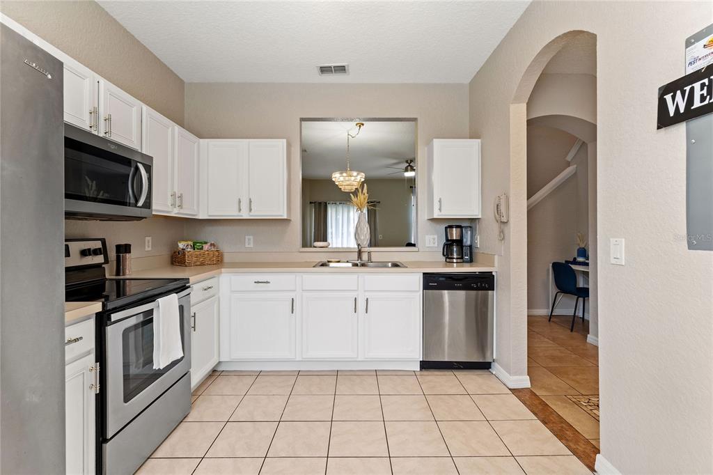 A kitchen features white cabinets, stainless steel appliances, and beige tile flooring — 436 CALABRIA AVENUE, DAVENPORT, FL