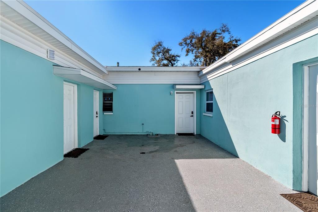 An exterior view of a turquoise building with a concrete courtyard and three white doors — 804 13TH AVENUE S, ST PETERSBURG, FL