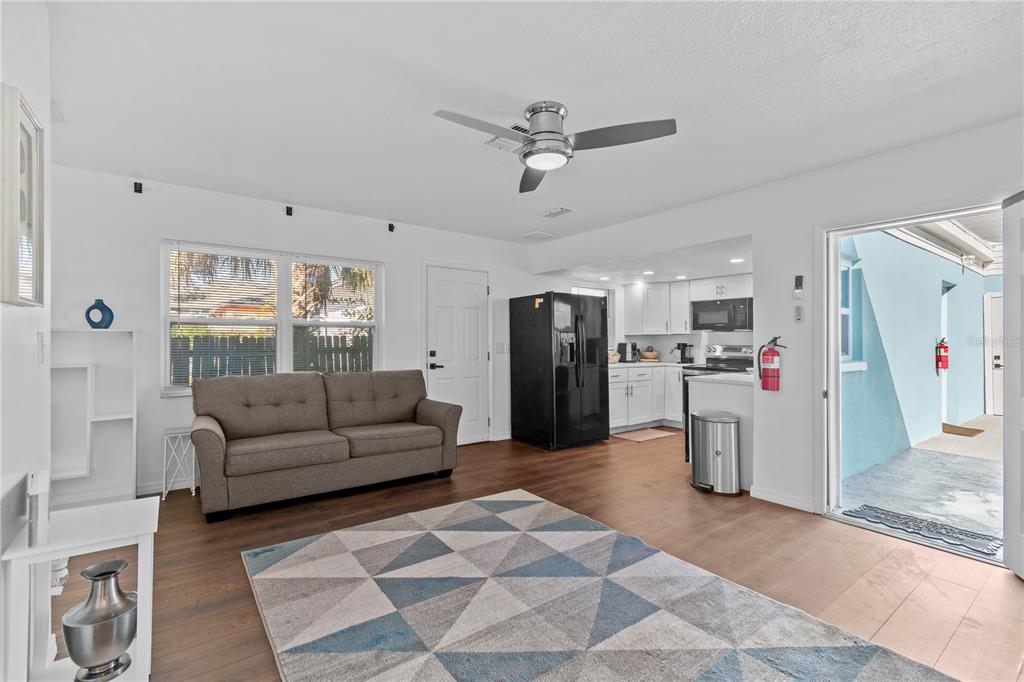 A living room with wood-look flooring, a grey sofa, a geometric rug, and an open kitchen — 804 13TH AVENUE S, ST PETERSBURG, FL