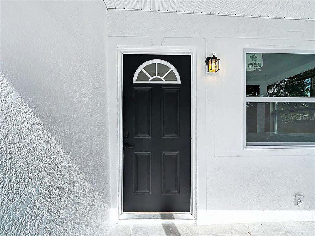 A black front door with a semi-circular window sits beside a window on a white porch — 402 E VIRGINIA AVENUE, TAMPA, FL