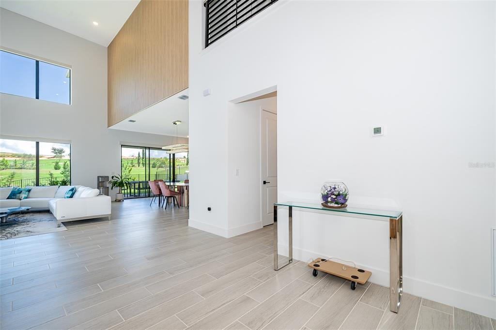 A bright, open-concept living area features white walls, light wood-look tile flooring, and high ceilings — 16046 VOLTERRA POINT, BELLA COLLINA, FL