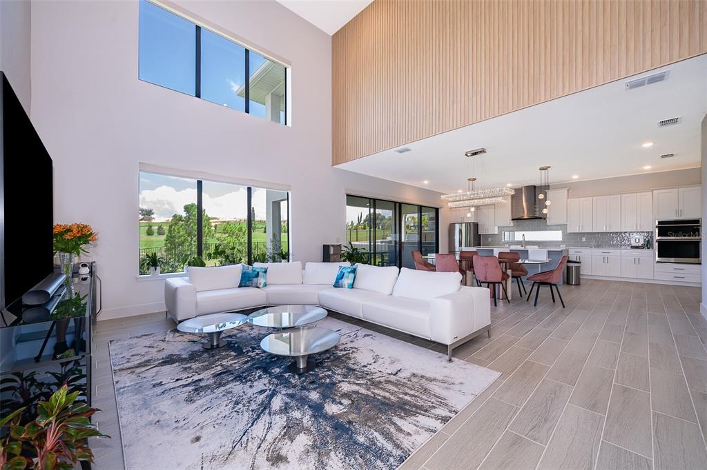 A modern open-concept living room and kitchen with high ceilings, tile floors, and large windows — 16046 VOLTERRA POINT, BELLA COLLINA, FL