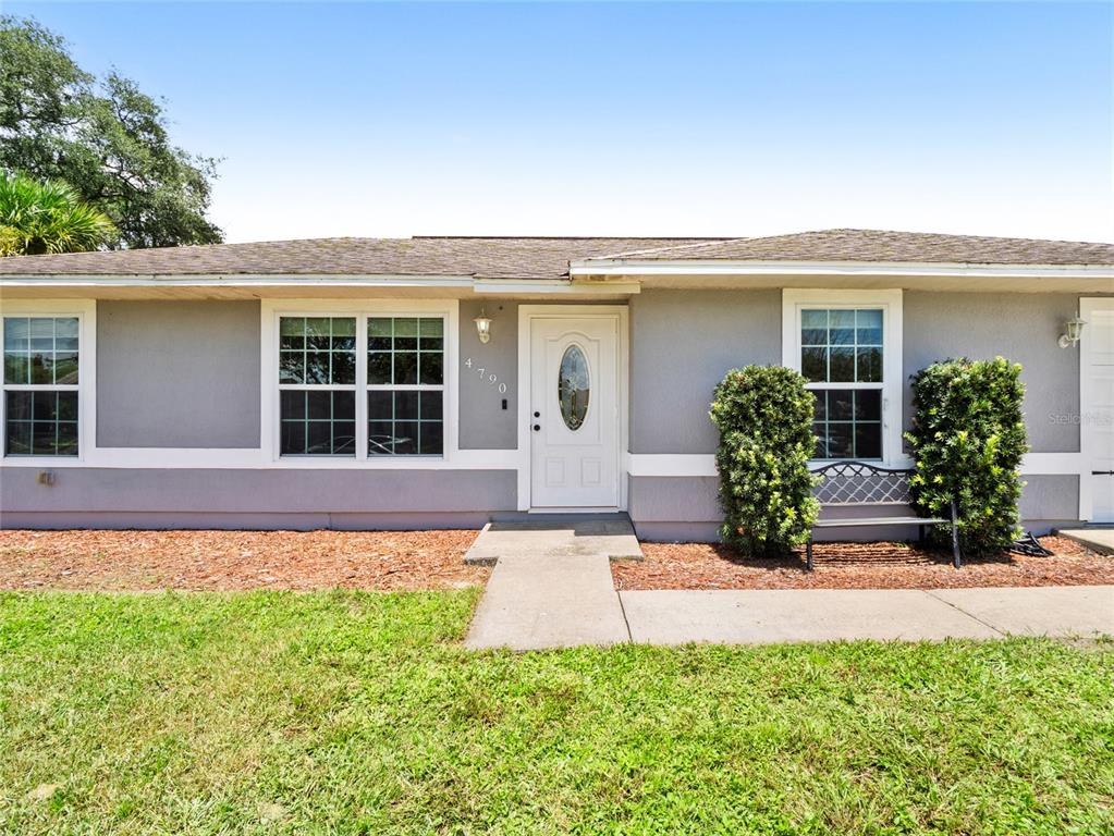 A single-story house with gray stucco siding, a white front door, and a concrete walkway — 4790 GREENHILL STREET, COCOA, FL