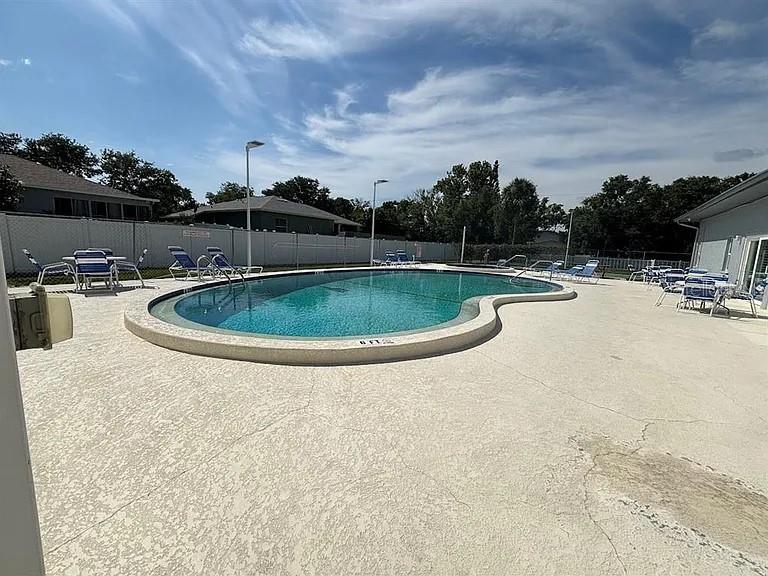 An outdoor swimming pool is surrounded by a concrete deck and lounge chairs — 10800 US HIGHWAY 19 N UNIT 237, PINELLAS PARK, FL