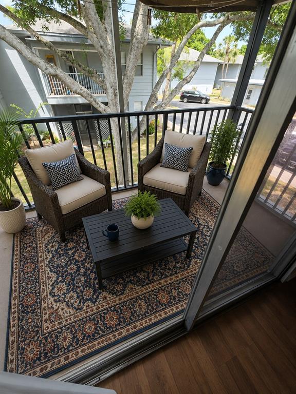 A screened balcony features two wicker chairs, a coffee table, and an area rug — 10800 US HIGHWAY 19 N UNIT 237, PINELLAS PARK, FL