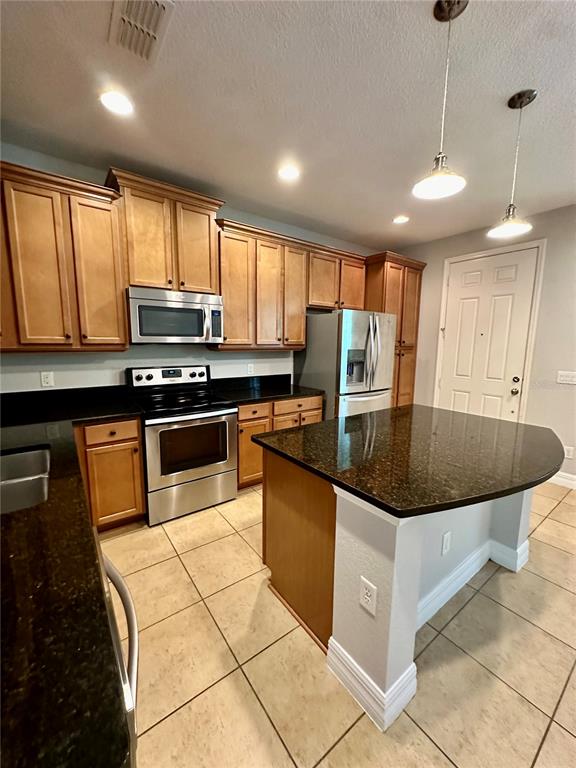 A kitchen features wood cabinets, stainless steel appliances, and a dark granite-topped island — 10083 EAGLE CREEK CENTER BOULEVARD, ORLANDO, FL