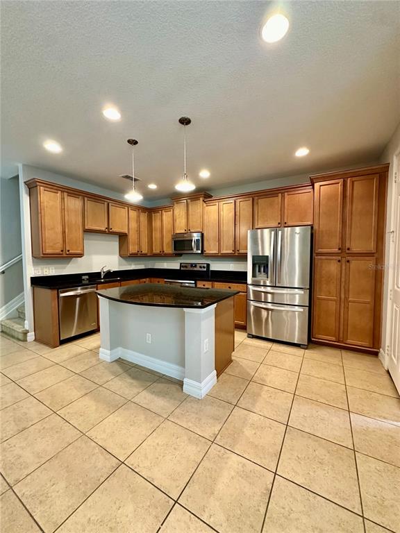 A kitchen features wooden cabinets, stainless steel appliances, a center island, and tiled flooring — 10083 EAGLE CREEK CENTER BOULEVARD, ORLANDO, FL
