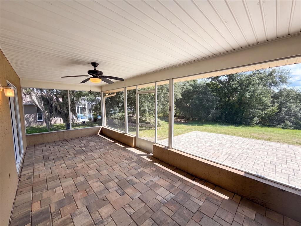 An empty room features light wood-look tile flooring, beige walls, a ceiling fan, and windows — 4573 BAYRIDGE COURT, SPRING HILL, FL