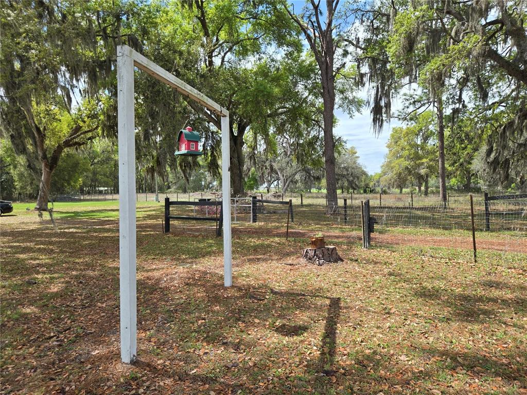 A red birdhouse hangs from a white wooden frame in a grassy, tree-filled yard — 2327 CR 528, SUMTERVILLE, FL