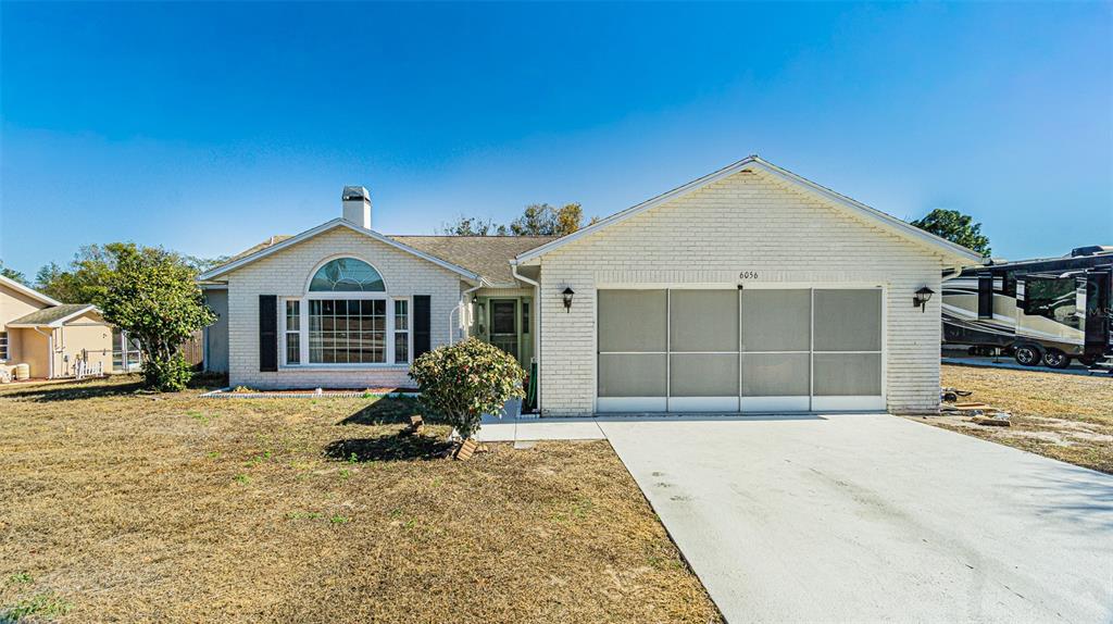 A single-story white brick house features a front-facing garage and a large arched window — 6056 SCHALEKAMP DRIVE, SPRING HILL, FL