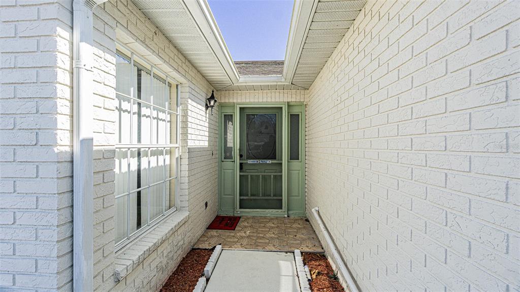A recessed entryway features a light green front door with sidelights and white brick walls — 6056 SCHALEKAMP DRIVE, SPRING HILL, FL