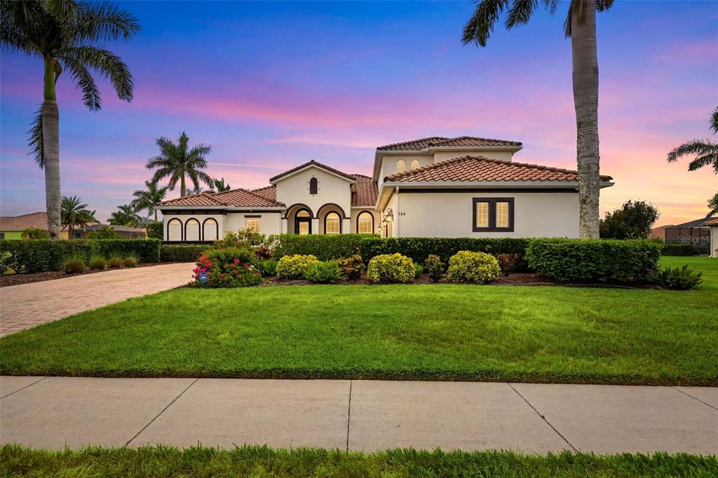 A single-story house with a tile roof, arched windows, and palm trees at sunset — 306 172ND STREET E, BRADENTON, FL