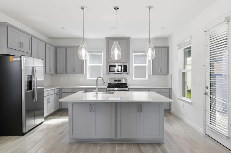 A modern kitchen features gray cabinets, a white quartz island, stainless steel appliances, and pendant lighting — 14751 FIELD DAISY DRIVE, WINTER GARDEN, FL