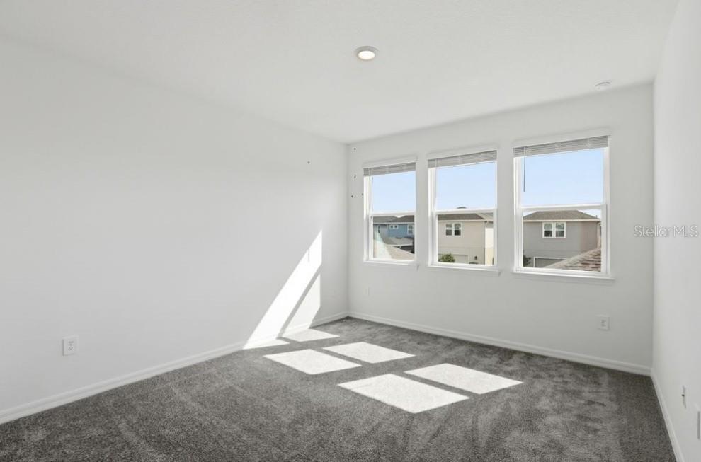 An empty bedroom with white walls, gray carpeting, and three windows overlooking neighboring houses — 14751 FIELD DAISY DRIVE, WINTER GARDEN, FL