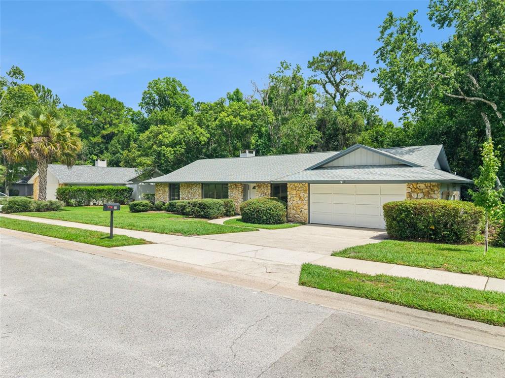A single-story house with a stone facade, a two-car garage, and a large front lawn — 211 HICKORY DRIVE, LONGWOOD, FL