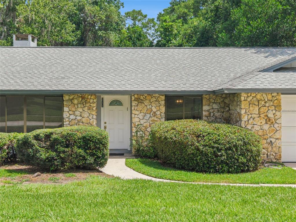 A single-story house with a stone facade, a white front door, and a shingled roof — 211 HICKORY DRIVE, LONGWOOD, FL