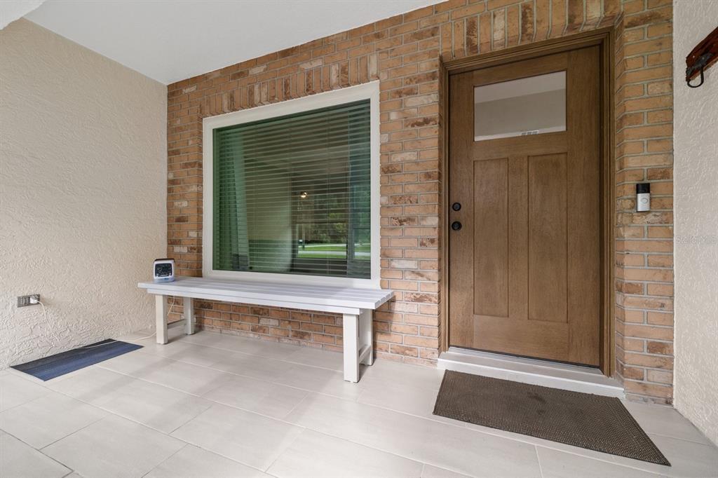 A front porch features a brick wall, a wooden door, a window, and a white bench — 12630 MAGNOLIA STREET, SAN ANTONIO, FL