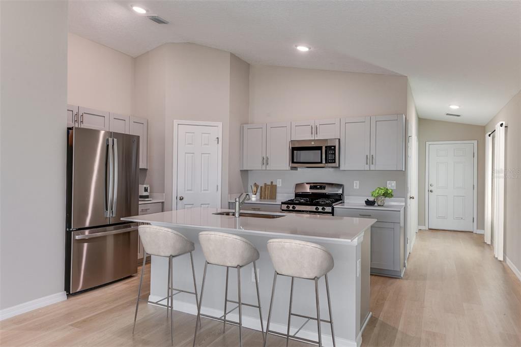 A modern kitchen features gray cabinets, stainless steel appliances, and a central island with seating — 15250 MAUDE LANDING LOOP, WIMAUMA, FL
