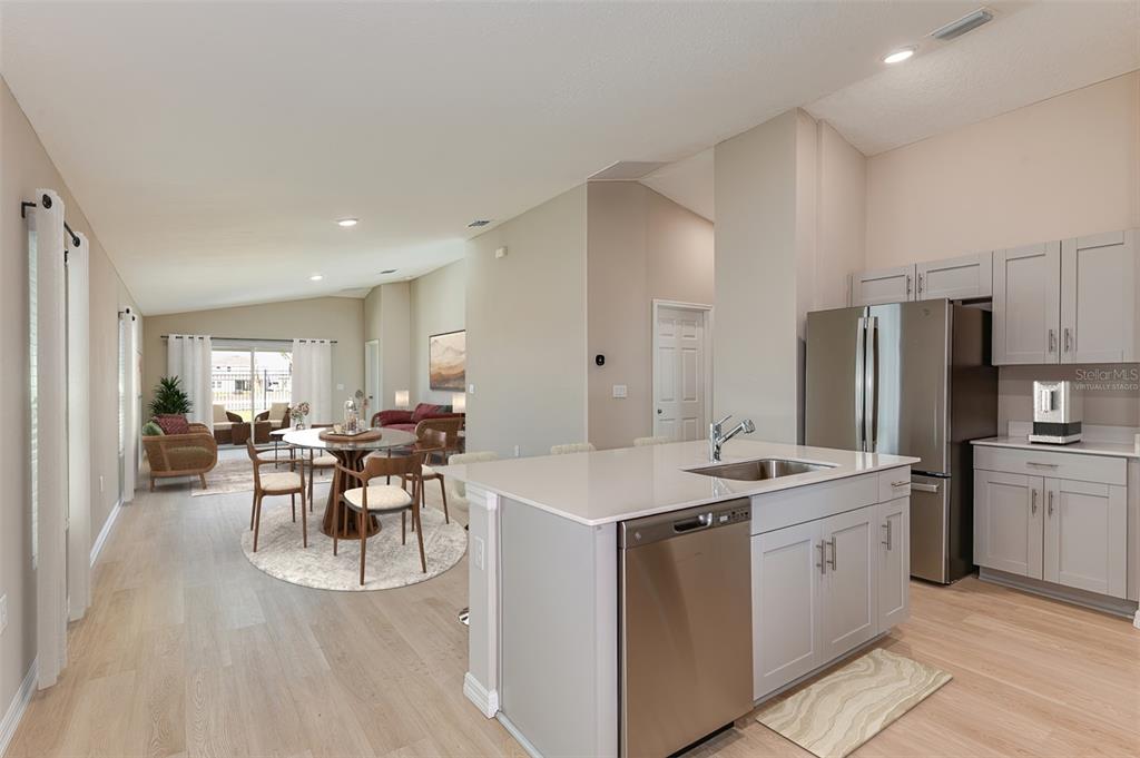 A kitchen with a center island and stainless steel appliances overlooks an open dining area — 15250 MAUDE LANDING LOOP, WIMAUMA, FL