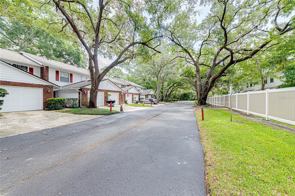 A paved street leads past a row of townhomes with garages and large oak trees — 5210 LAZY OAKS DRIVE, WINTER PARK, FL