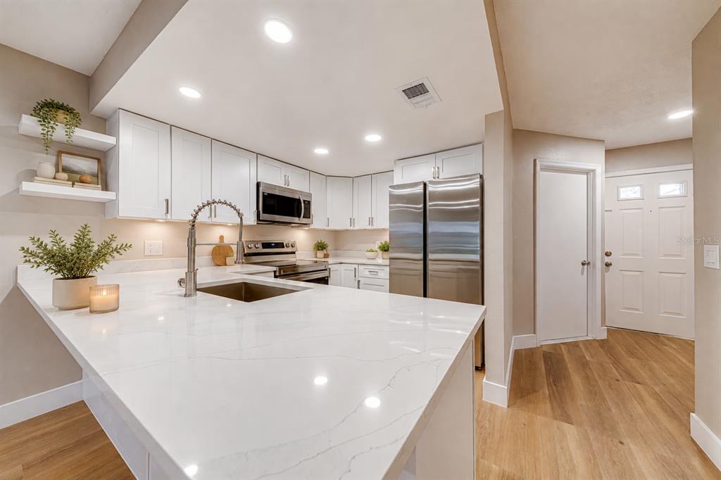 A modern kitchen features white cabinets, stainless steel appliances, and a large quartz-topped island — 5210 LAZY OAKS DRIVE, WINTER PARK, FL